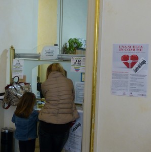 Foto dello sportello dell’Anagrafe con la locandina della campagna di comunicazione “Una scelta in Comune”